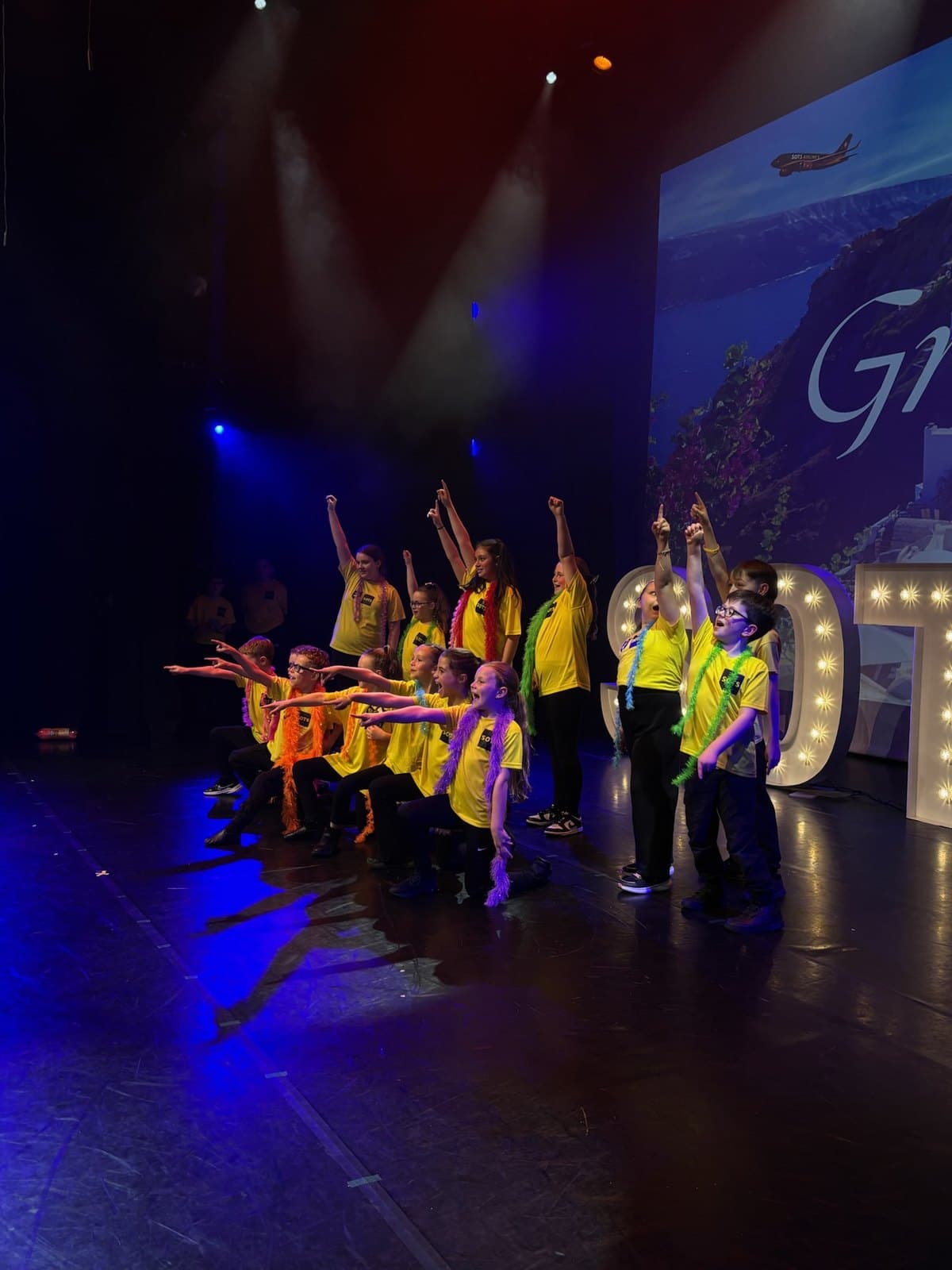 Act Two Musical Theatre students in yellow Stand-Out t-shirts performing on stage with SOTS light-up letters
