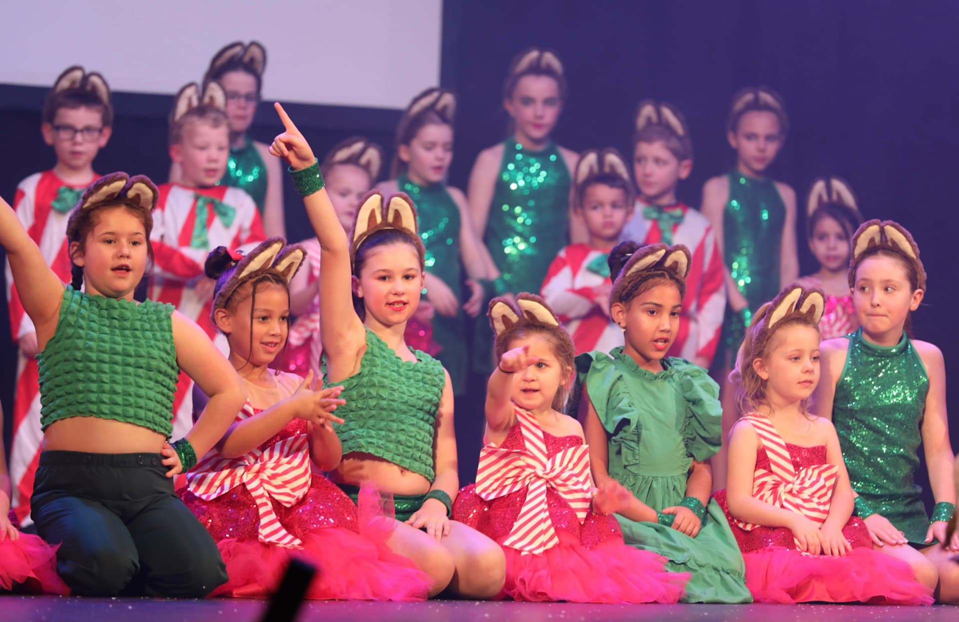 Kids on stage in red and green sequined Christmas costumes with bunny ears