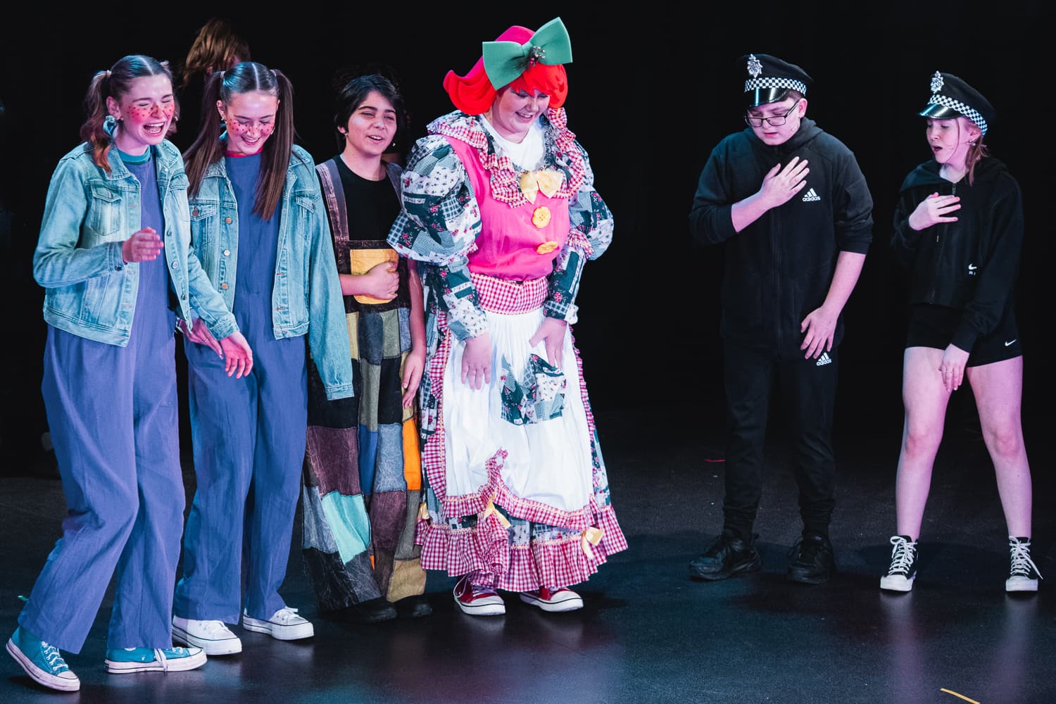 Pantomime cast on stage including the dame character mid-scene