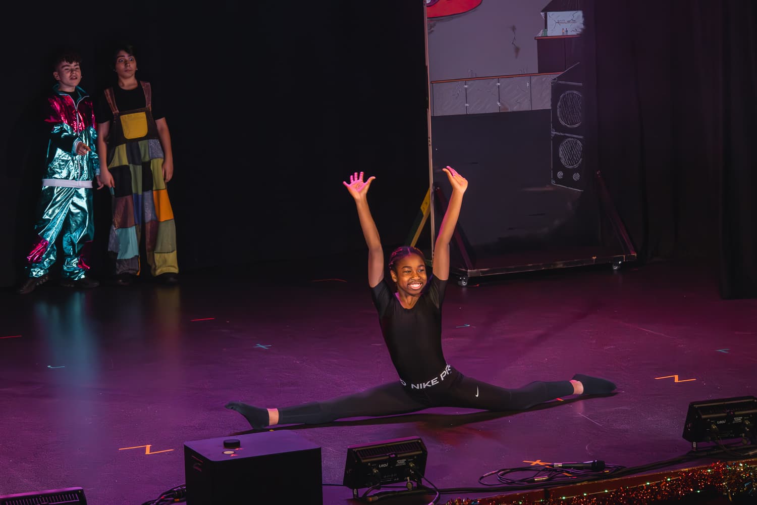 Senior performer mid-splits on stage with dramatic purple lighting during the Christmas pantomime