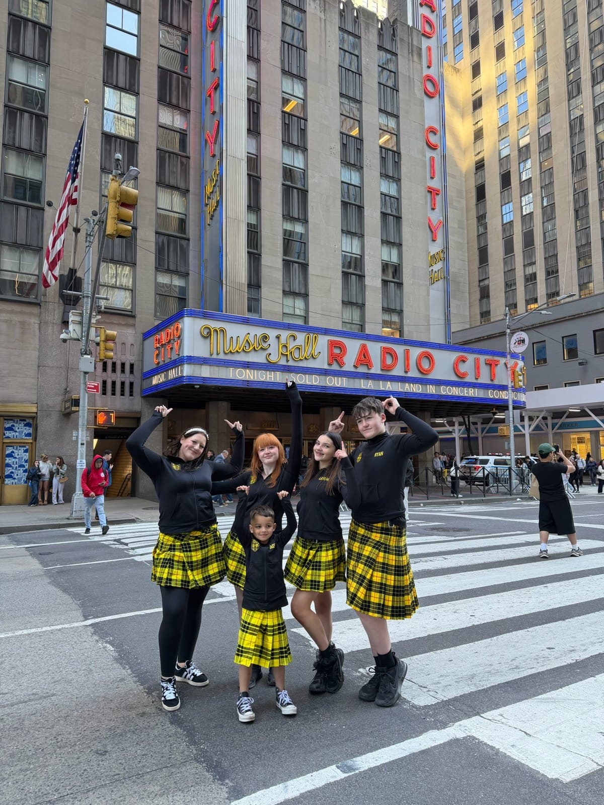 SOTS students in yellow tartan kilts posing outside Radio City Music Hall in New York