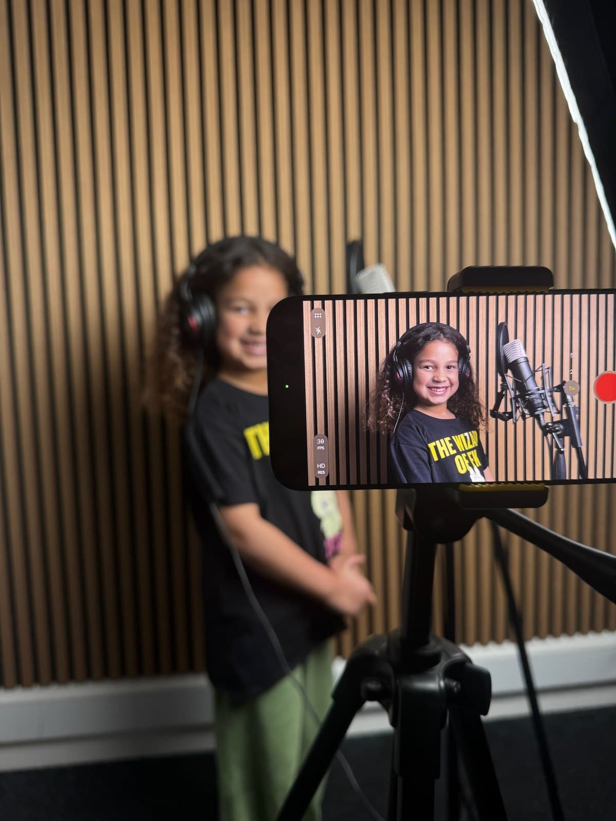 Young Stand-Out student smiling in the recording studio, framed on a phone on a tripod