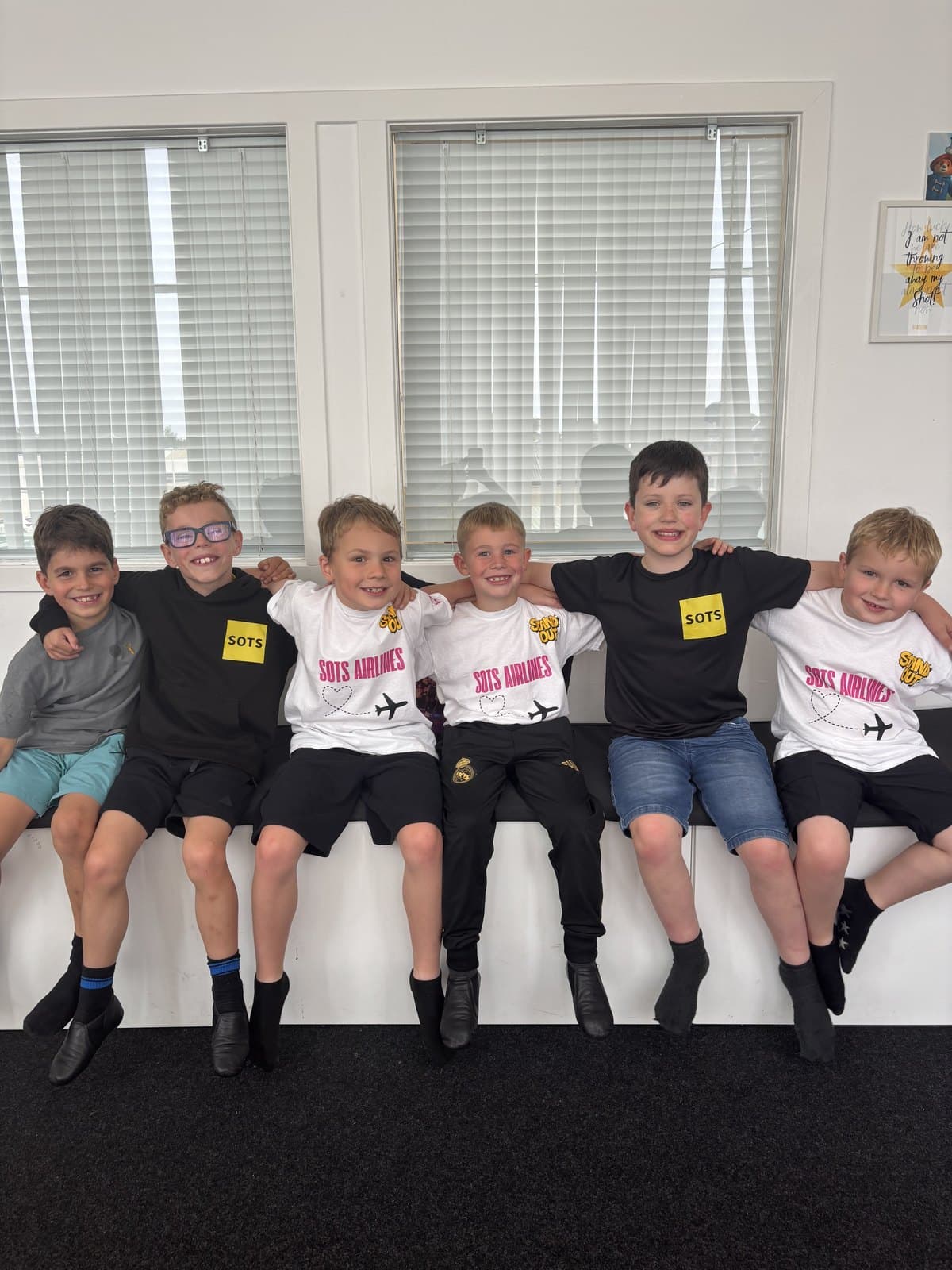 Six young SOTS students sitting together on a studio bench in SOTS Airlines t-shirts