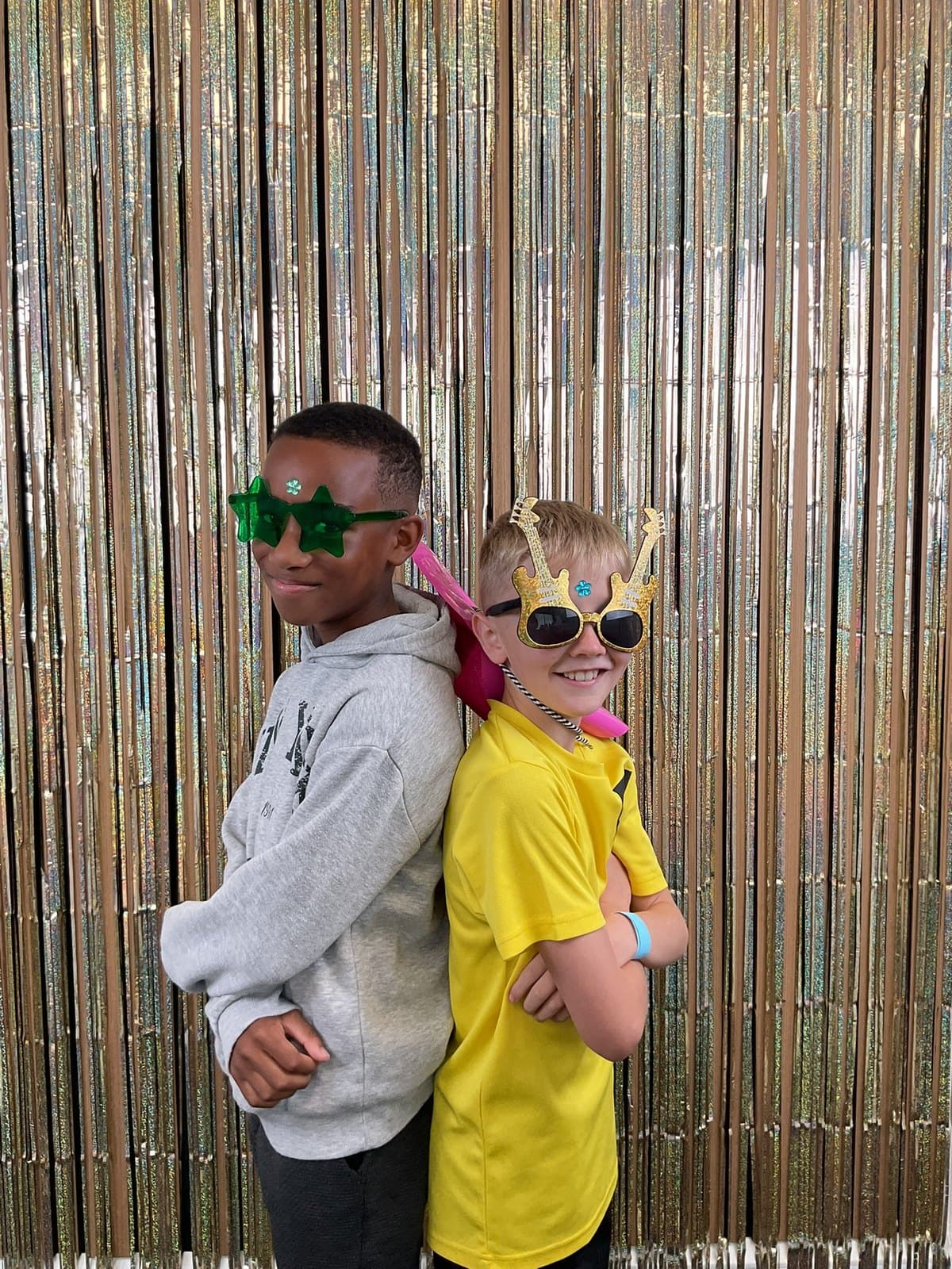 Two students back to back in novelty sunglasses in front of a gold tinsel curtain at SOTS Fest