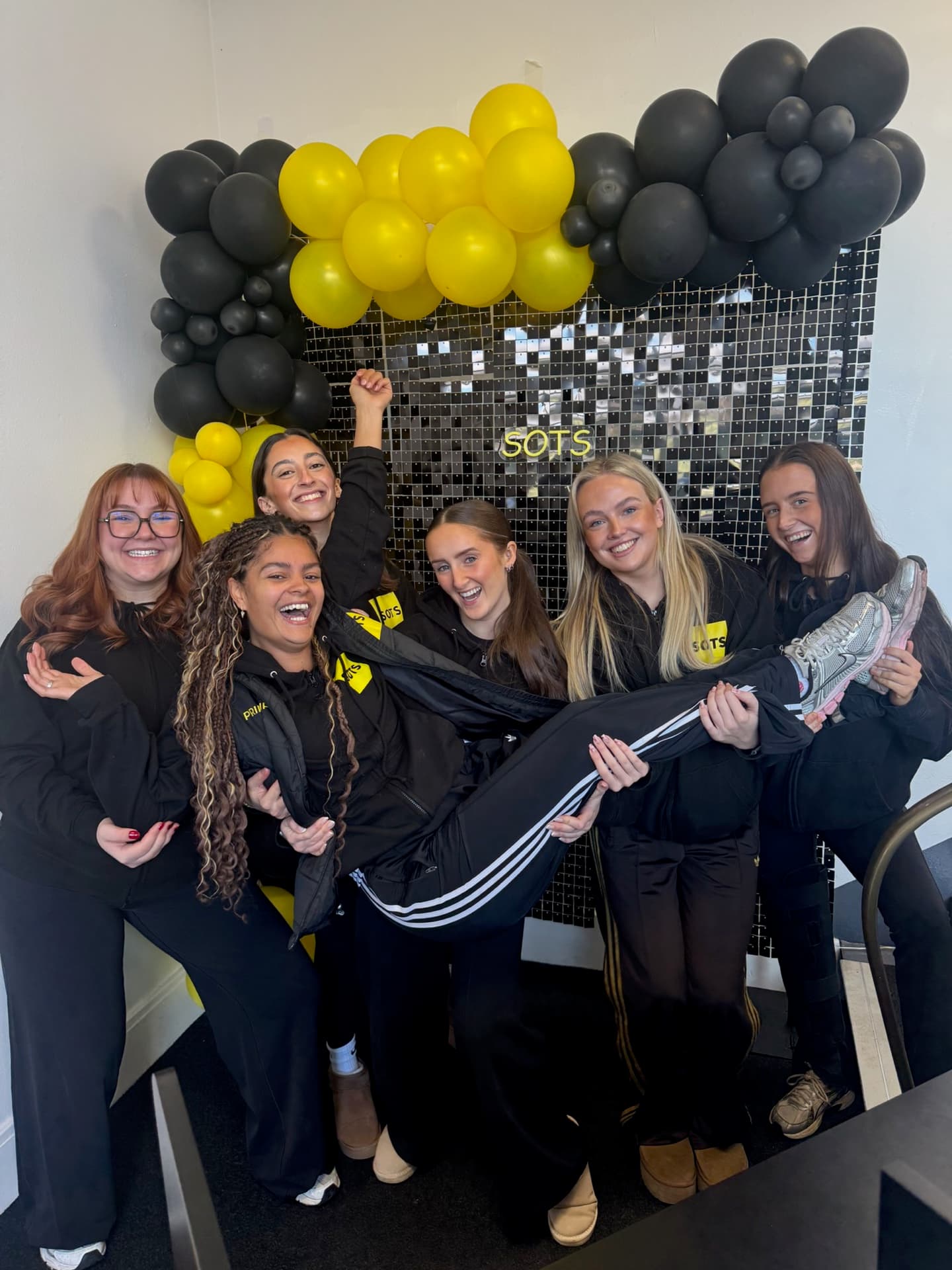 Stand-Out studio team in front of the SOTS shimmer wall with yellow and black balloons