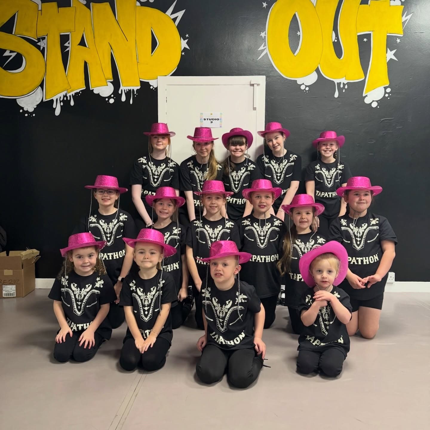 Tap-a-thon troupe in pink hats in front of the STAND OUT graffiti wall